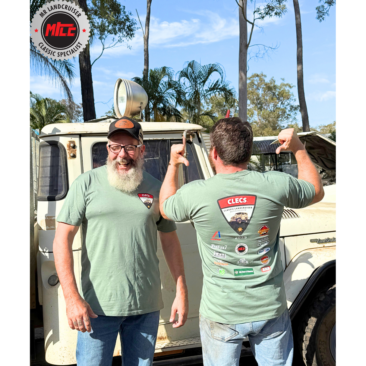 Two men wearing CLECS 2025 green t-shirts with a brand logo, standing in front of a vintage vehicle with trees in the background.