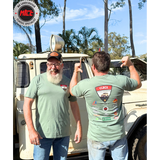 Two men wearing CLECS 2025 green t-shirts with a brand logo, standing in front of a vintage vehicle with trees in the background.